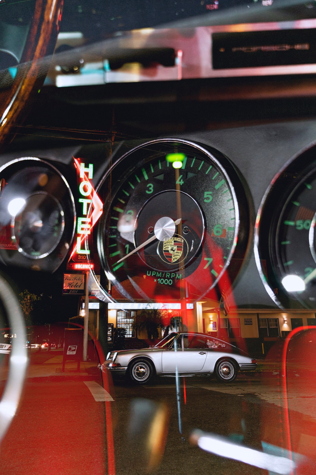 Gauges and a neon hotel sign reflected through the windshield at night